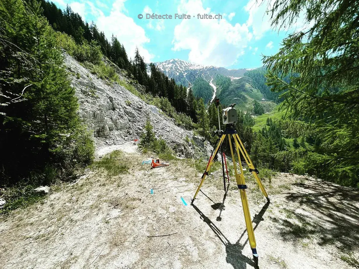 Instrument de relevé sur trépied à côté de repères bleus sur un chemin de montagne